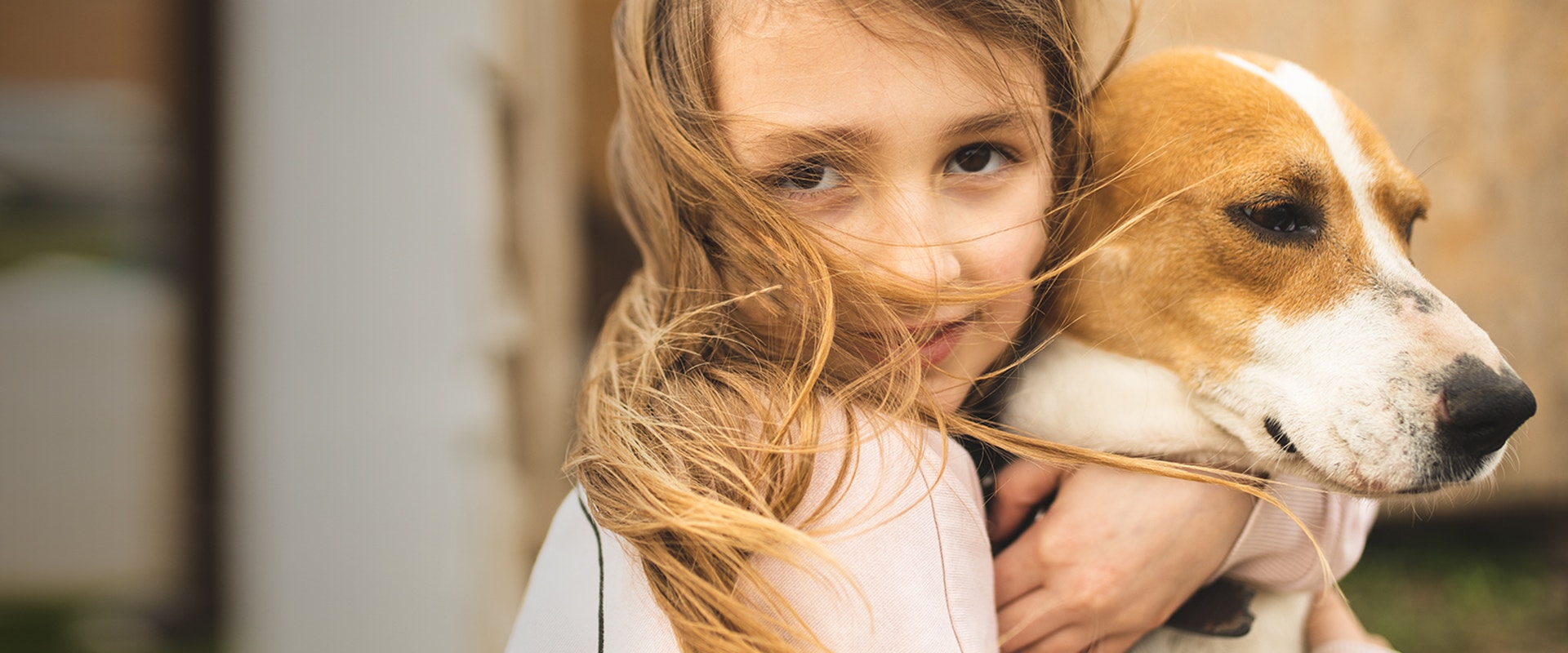 Niña pequeña abrazando a un perro en un ambiente exterior, destacando el vínculo entre humanos y mascotas.